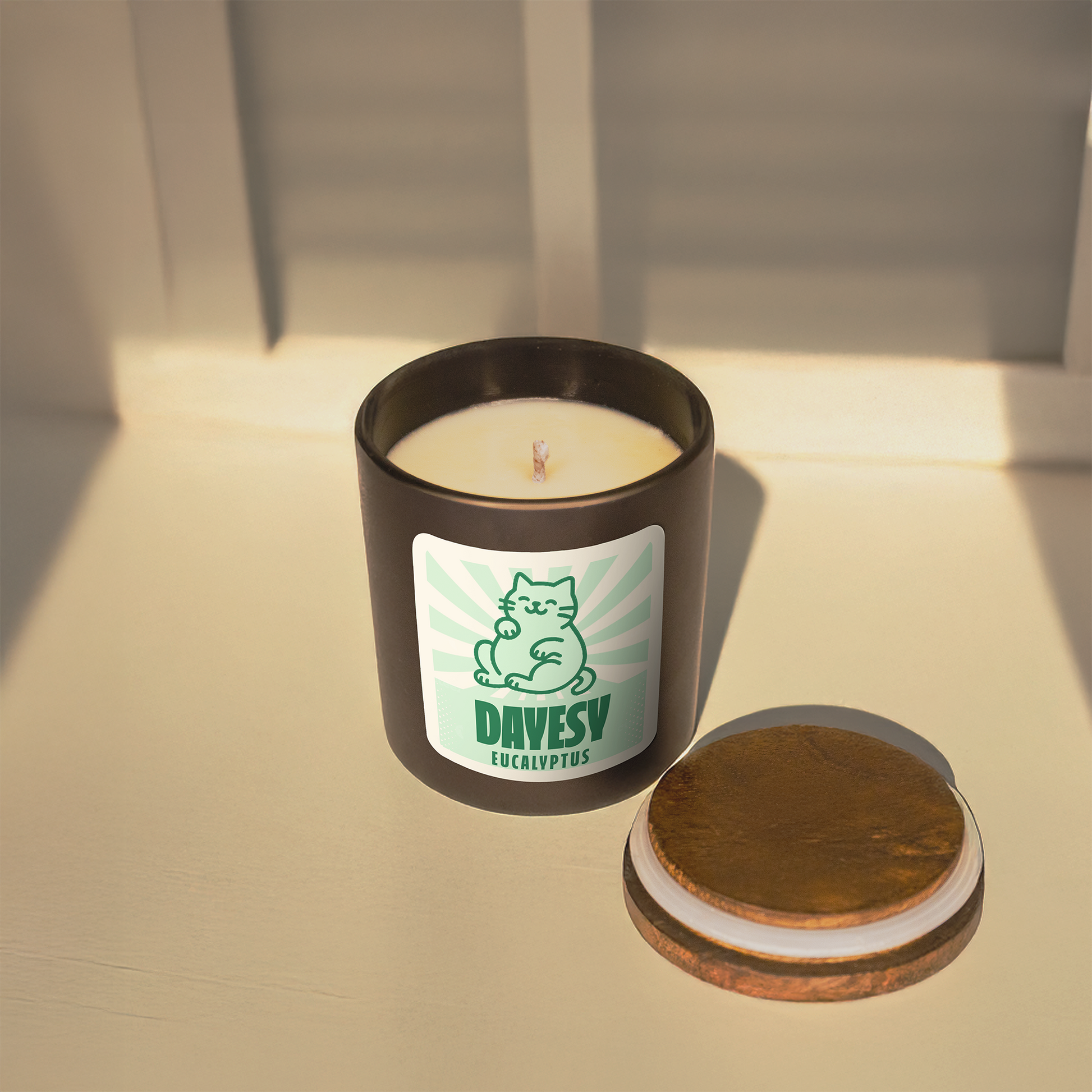 Candle in a black container with a label featuring a cat illustration on a light surface.