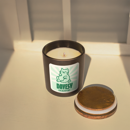 Candle in a black container with a label featuring a cat illustration on a light surface.