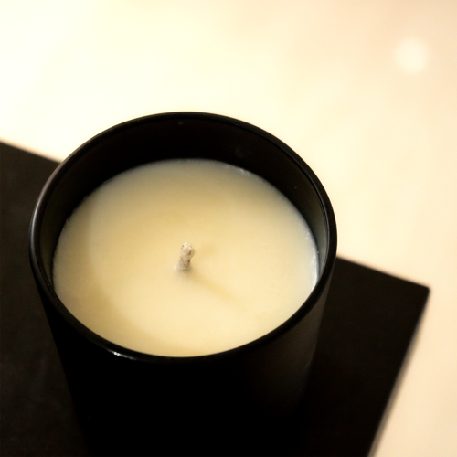 White candle in a black container on a dark surface with a blurred background